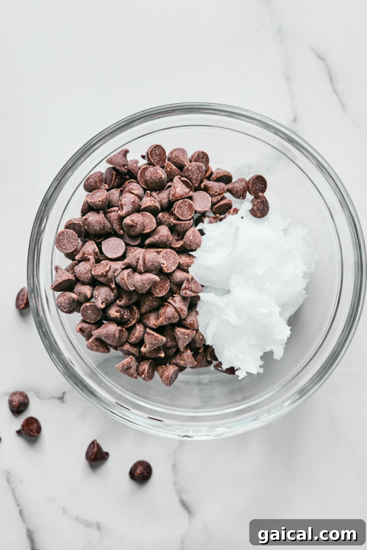Create Your Own Magical Chocolate Coating 3 A glass bowl filled with chocolate chips and a dollop of coconut oil on a marble surface.