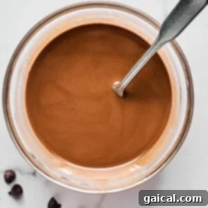 Bowl of melted chocolate with a metal spoon, placed on a white marble surface next to a few chocolate chips.