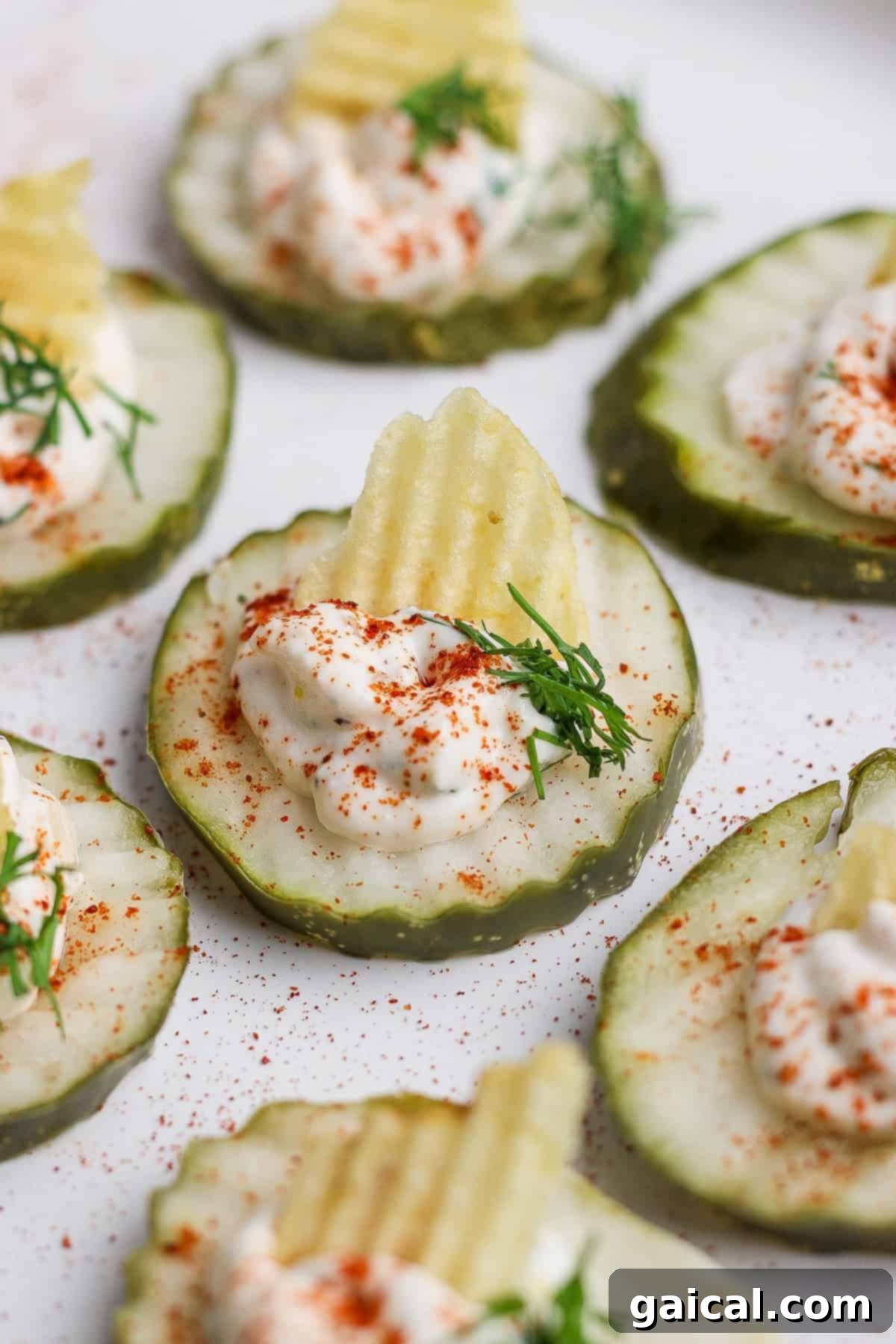 Cucumber slices topped with creamy dip, a potato chip, dill, and sprinkled with paprika, ready to be served as deviled pickles.