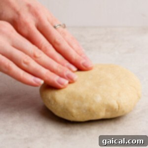 A pair of hands gently presses down on a perfectly rounded ball of fresh dough, positioned on a sleek gray countertop, illustrating the tactile process of shaping dough for baking.