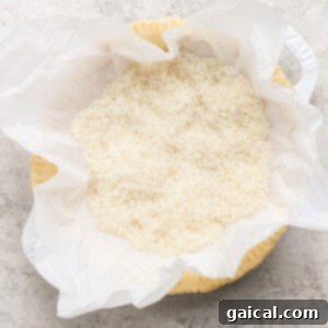 A baking bowl, meticulously lined with parchment paper, is filled to the brim with uncooked white rice, strategically placed on a textured surface to illustrate the process of blind baking.