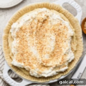 A meticulously decorated pie, featuring luscious whipped cream and toasted coconut flakes, presented on a light-colored surface with a precision knife and an elegant striped cloth positioned nearby, ready for serving.