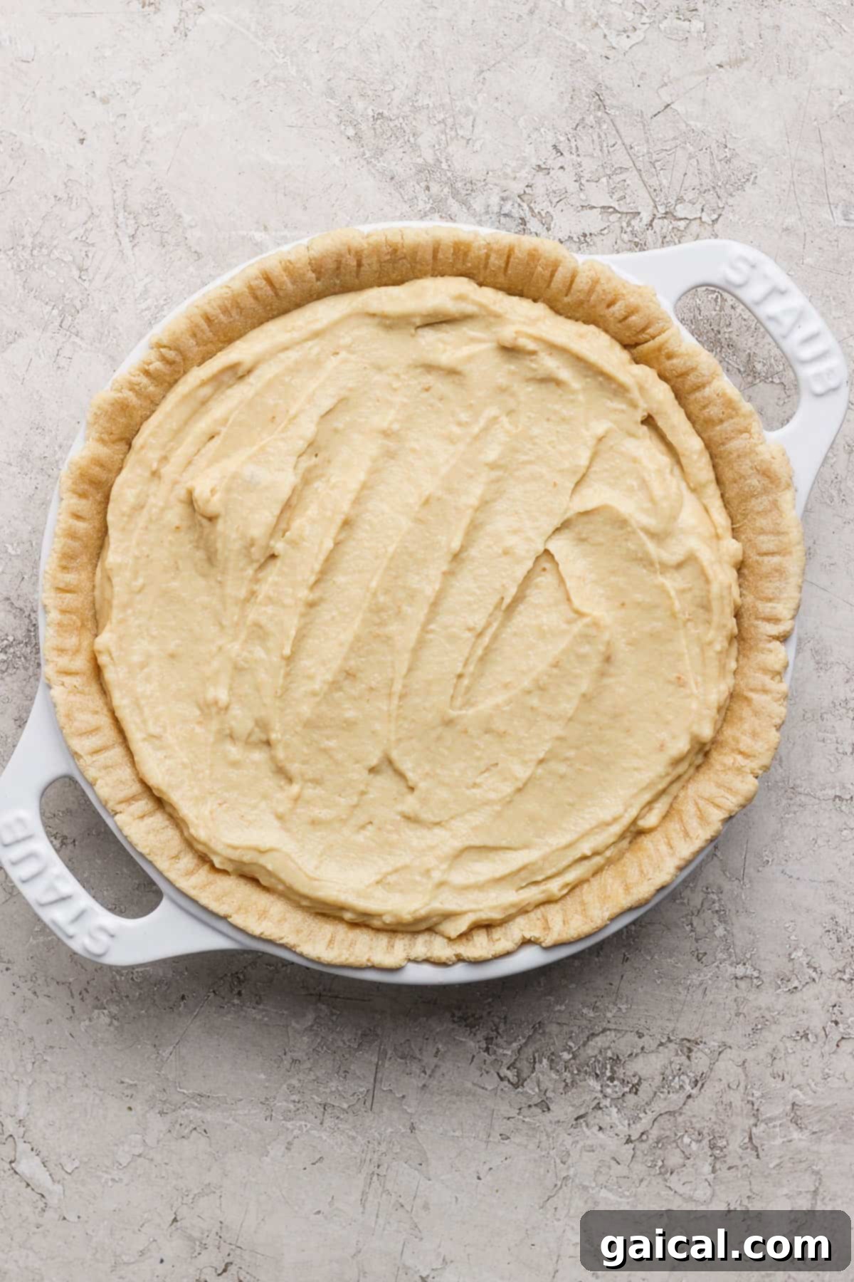 Luscious Coconut Cream Pie 4 An unbaked pie crust, delicately cradling a rich, creamy batter within a pristine white baking dish, set against a subtly textured surface, awaiting its transformation in the oven.