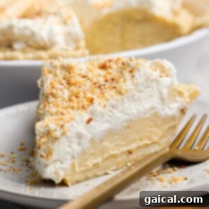 A beautifully presented slice of coconut cream pie on a white plate with a gold fork, crowned with fluffy whipped cream and toasted coconut flakes, ready to be savored.