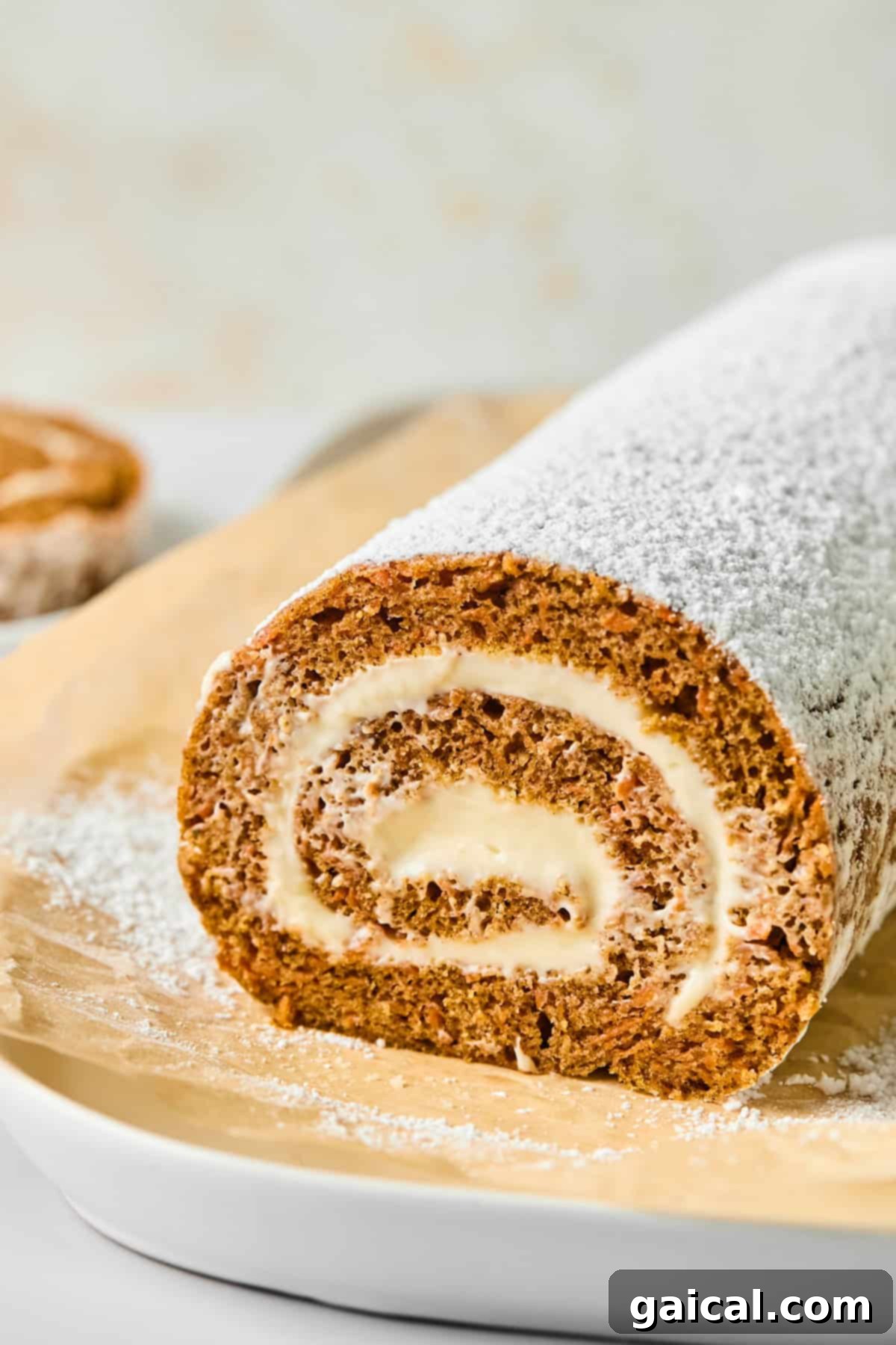 Protein-Packed Carrot Cake Roll 2 A beautifully rolled carrot cake dusted with powdered sugar on parchment paper, revealing a delicious spiral of creamy, protein-packed filling.
