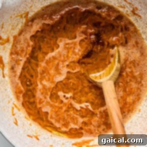 Protein-Packed Carrot Cake Roll 10 A white bowl filled with a frothy, orange mixture, and a wooden spoon partially immersed in the liquid, resting against the side.