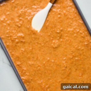 Protein-Packed Carrot Cake Roll 11 Baking tray filled with raw carrot cake batter and a spatula resting on top.