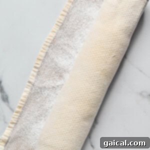 Protein-Packed Carrot Cake Roll 13 Rolled-up dough wrapped in a floured kitchen towel on a marble surface.