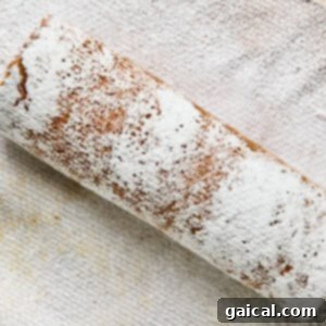 Protein-Packed Carrot Cake Roll 16 A rolled cake dusted with powdered sugar rests on a textured cloth.