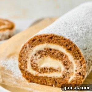 Protein-Packed Carrot Cake Roll 17 A rolled cake dusted with powdered sugar on parchment paper, showing a spiral of cream filling.