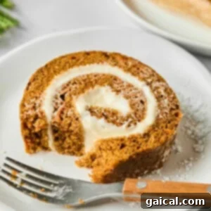A slice of pumpkin roll with cream cheese filling on a white plate, partially eaten, with a fork beside it.