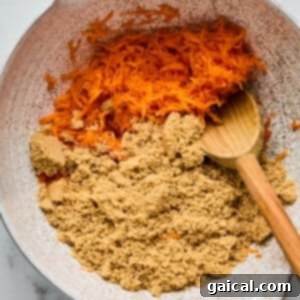 Protein-Packed Carrot Cake Roll 7 A mixing bowl containing shredded carrots and brown sugar, with a wooden spoon resting inside.