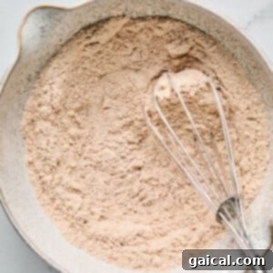Protein-Packed Carrot Cake Roll 8 A bowl of dry ingredients is mixed with a metal whisk on a marble surface.