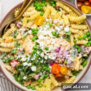 Creamy Roasted Red Pepper Pasta Delight 7 Bowl of pasta salad with rotini, peas, cherry tomatoes, crumbled cheese, greens, and a creamy dressing, garnished with chopped onions and red pepper flakes.