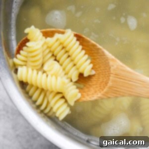 A wooden spoon holding cooked rotini pasta above a pot of boiling water.