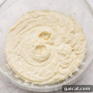 Layered Coconut Bliss with Fresh Raspberries 7 A glass bowl filled with creamy, light yellow cake batter, perfectly smooth and ready for baking, resting on a textured white surface.