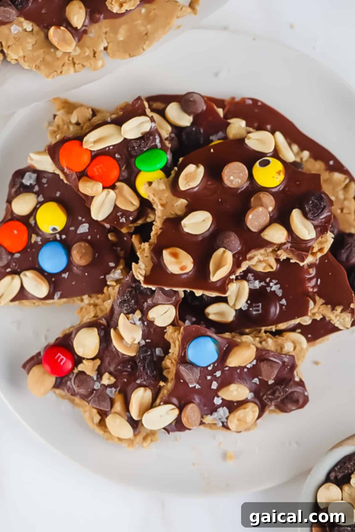 Protein Packed Cookie Dough Bark 3 A plate of peanut butter and chocolate bark topped with colorful candy-coated chocolates, peanuts, and sea salt flakes, on a white surface, showcasing its delicious texture.