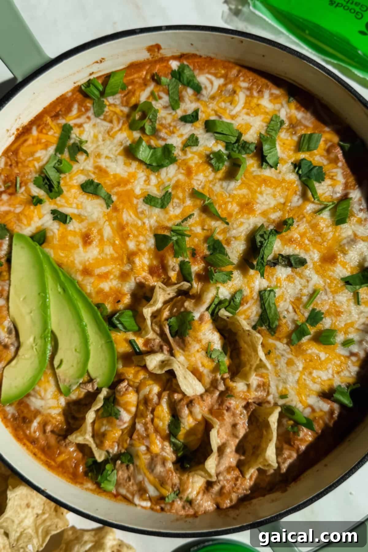 Beefy Cottage Queso 2 A dish of cheesy dip topped with fresh cilantro and avocado slices in a white casserole dish, surrounded by golden tortilla chips.