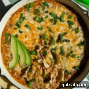Beefy Cottage Queso 5 A baked dish of ground beef cottage cheese queso topped with melted cheese, garnished with sliced avocado and fresh herbs, served next to tortilla chips.