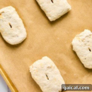 Four unbaked biscuit dough pieces, reminiscent of bubbling pizza crusts, rest on a parchment-lined baking sheet.