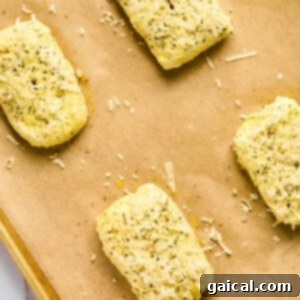 Four rectangular pizza hot pockets of seasoned dough rest on a parchment-lined baking sheet, sprinkled with herbs and cheese.
