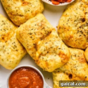 Golden, herb-seasoned bread parcels resembling mini pizza hot pockets sit beside a small dish of sliced pepperoni and a cup of marinara sauce.