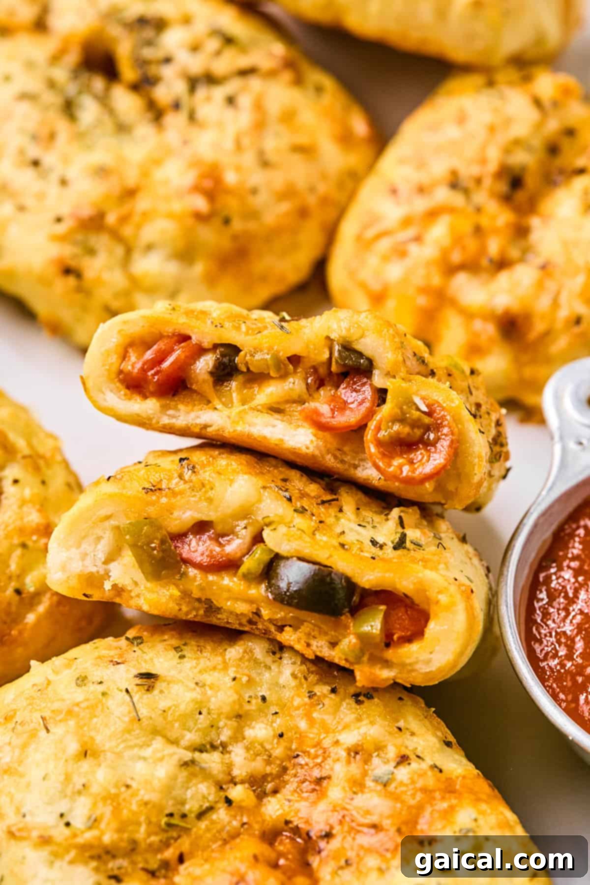 Close-up of baked calzones, reminiscent of pizza hot pockets, filled with cheese, pepperoni, and vegetables, accompanied by a small dish of marinara sauce.