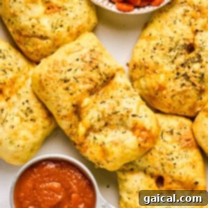 Golden-brown stuffed bread rolls, reminiscent of delightful pizza hot pockets, are sprinkled with herbs and paired with a small bowl of tomato sauce on a white surface.