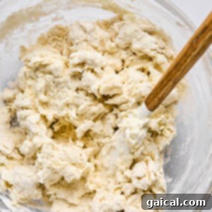 A glass bowl containing partially mixed dough with a wooden spoon sits ready to become delicious homemade pizza or hot pockets.