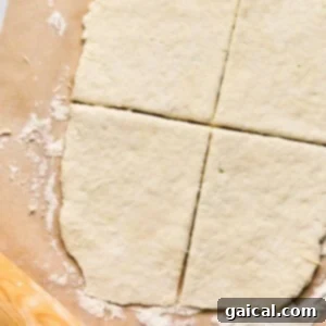 Rolled-out dough on parchment paper, cut into four sections like the perfect start for homemade pizza pockets, with a wooden rolling pin nearby.