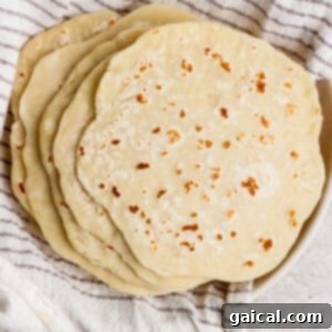 A comforting stack of freshly made homemade flatbreads rests nestled within a striped kitchen towel, keeping them warm and soft.