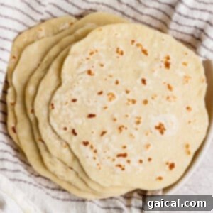 A stack of homemade flour tortillas rests on a striped kitchen towel, ready for use.