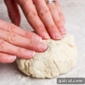 Hands gently kneading a soft ball of dough on a generously floured surface, demonstrating the process of achieving a smooth consistency.