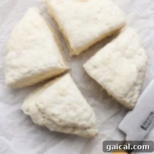 Four equal wedges of raw, unbaked dough and a knife with a wooden handle resting on white parchment paper, illustrating the dividing process before rolling.