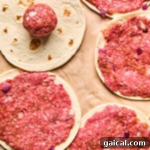 Zesty Street Corn Smash Tacos 10 Round pieces of flatbread topped with seasoned raw ground meat and chopped onions are arranged on parchment paper, with one meatless flatbread and a raw meatball visible.