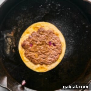 Zesty Street Corn Smash Tacos 11 A corn tortilla with refried beans and a few pieces of red onion is cooking in a black cast-iron skillet.