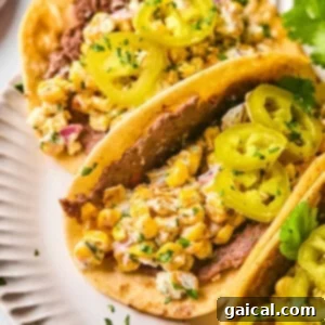 Zesty Street Corn Smash Tacos 13 Two tacos on a white plate filled with refried beans, corn salad, and topped with sliced pickled jalapeños and chopped herbs.