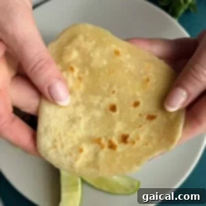 Zesty Street Corn Smash Tacos 3 Two hands hold a flatbread over a plate containing lime wedges.