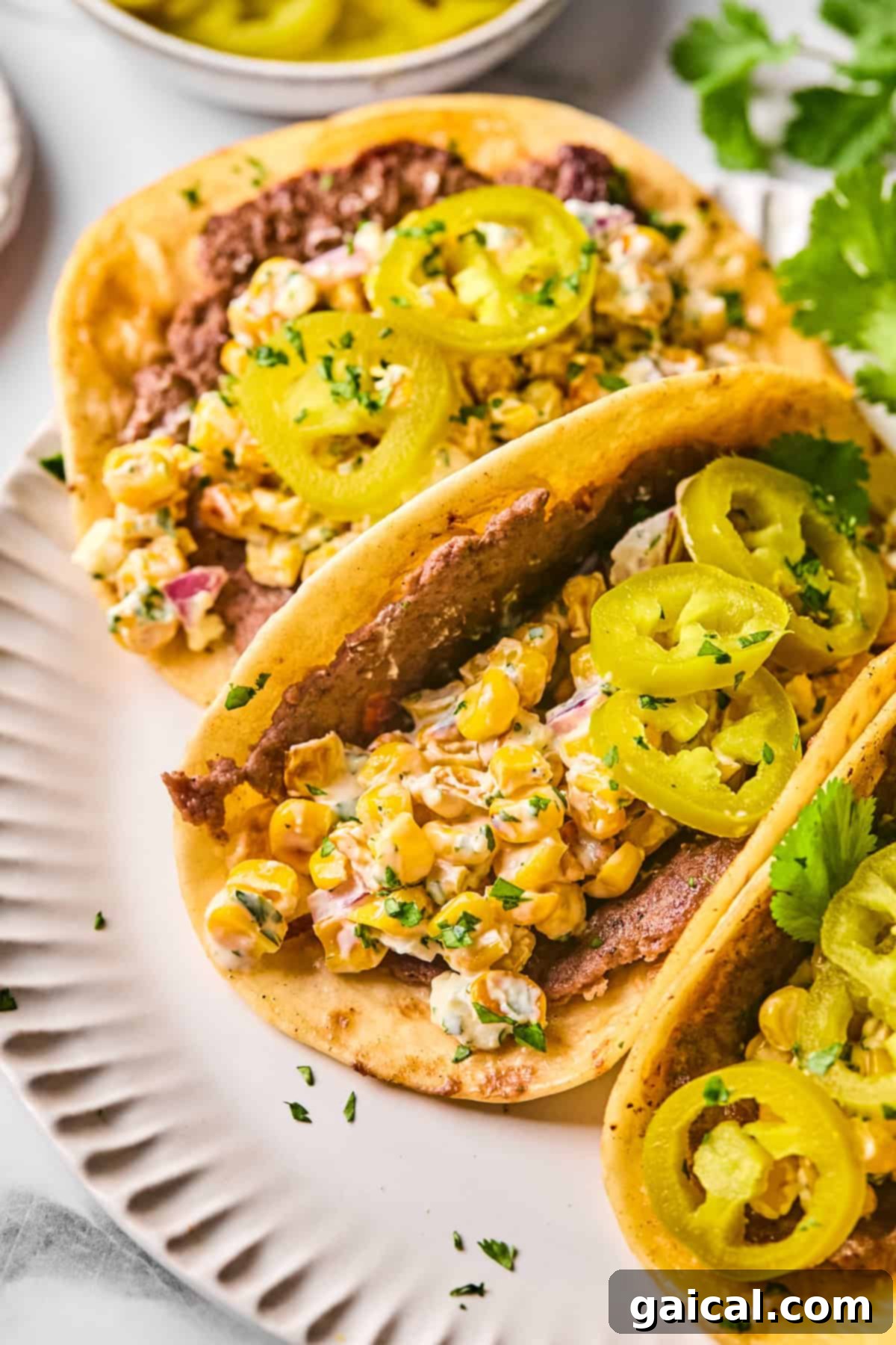 Zesty Street Corn Smash Tacos 5 Two Street Corn Smash Tacos on a white plate, showcasing a delightful blend of refried beans and creamy corn salad, garnished with vibrant sliced pickled jalapeños and fresh chopped herbs.