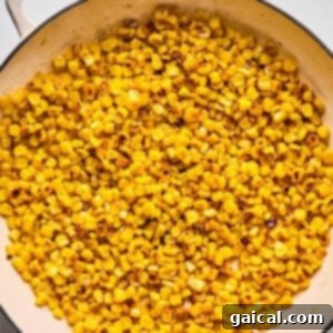 Zesty Street Corn Smash Tacos 8 A skillet filled with sautéed corn kernels on a white marble surface.