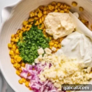 Zesty Street Corn Smash Tacos 9 A bowl contains corn, chopped cilantro, diced red onion, crumbled cheese, mayonnaise, and sour cream, ready to be mixed.