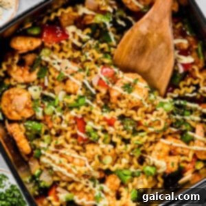 A pan filled with cooked pasta, shrimp, vegetables, and herbs being stirred with a wooden spatula.