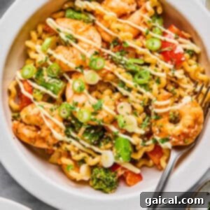 Crispy Air Fryer Shrimp and Roasted Vegetables 8 A bowl of pasta with shrimp, broccoli, red bell peppers, and green onions, drizzled with a creamy sauce and served with a fork.