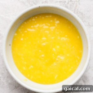 A white bowl filled with beaten eggs on a textured white surface.