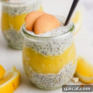 Glass jar filled with chia seed pudding and lemon layer, topped with two cookies and a spoon. Lemon slices are in the background.