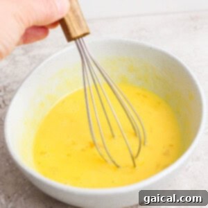 Hand whisking yellow batter in a gray bowl.