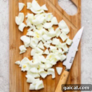 Chopped boiled eggs on a wooden cutting board with a knife on the side, placed on a light-colored surface.