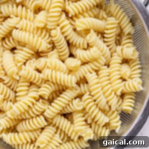 Cooked rotini pasta draining in a stainless steel colander.