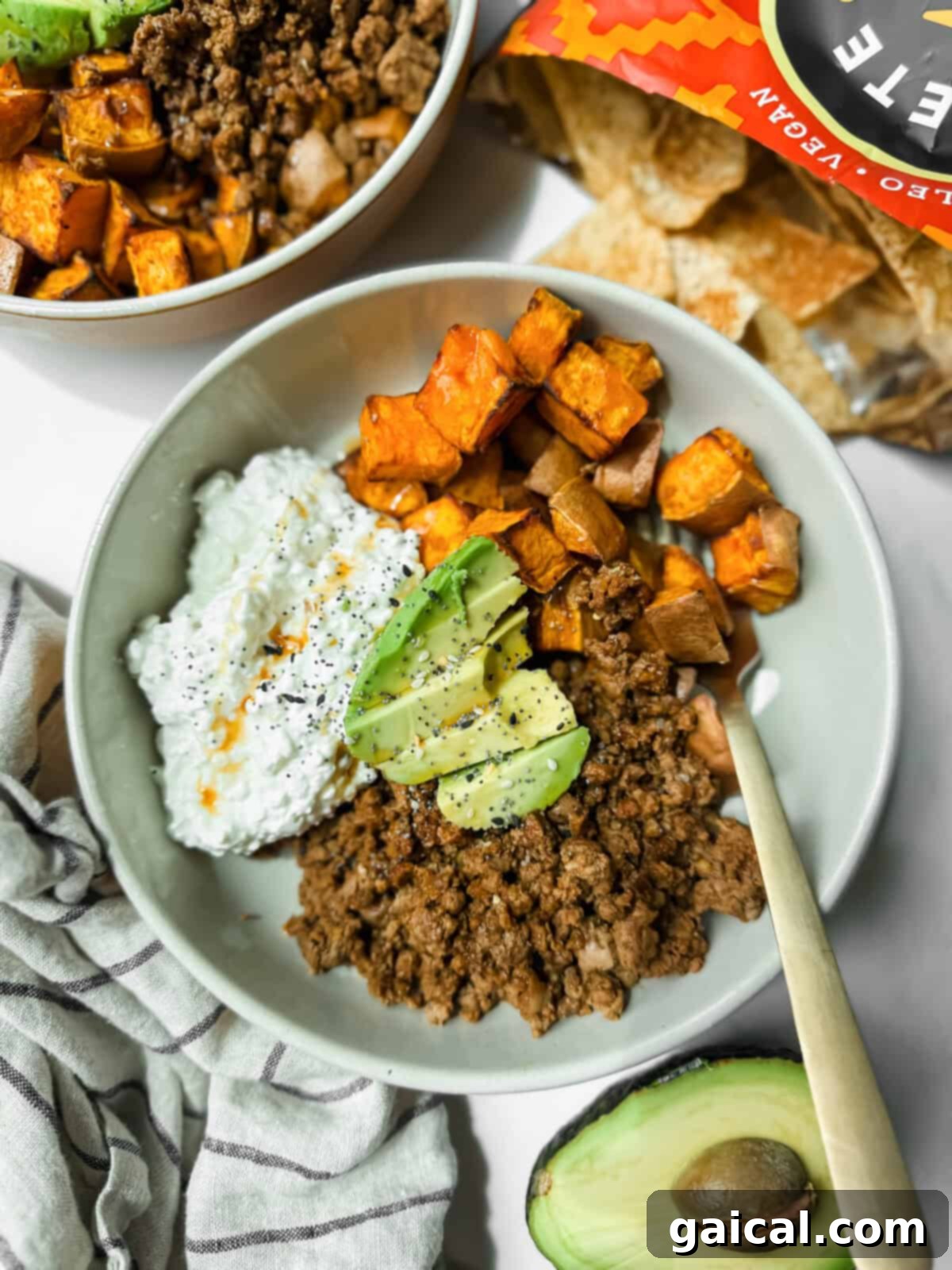 The Ultimate Hot Honey Ground Beef Sweet Potato Bowl with Cottage Cheese 2 A bowl with ground beef, roasted sweet potatoes, cottage cheese, and avocado slices sits next to an open bag of tortilla chips and a halved avocado.