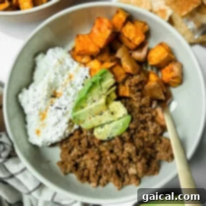 A bowl containing ground beef, roasted sweet potatoes, cottage cheese with hot sauce, and avocado slices, topped with black pepper.